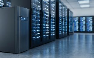 Modern bir veri merkezinin koridorunda, sunucu raflarının yanında duran büyük, endüstriyel bir Kesintisiz Güç Kaynağı (UPS) ünitesi. Arka plandaki sunucuların ışıkları bulanık bir şekilde parlıyor.